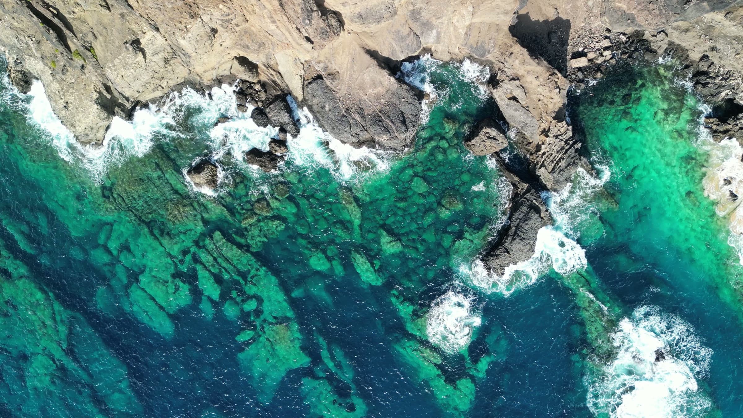 Aerial view of turquoise water breaking over a rocky coastline