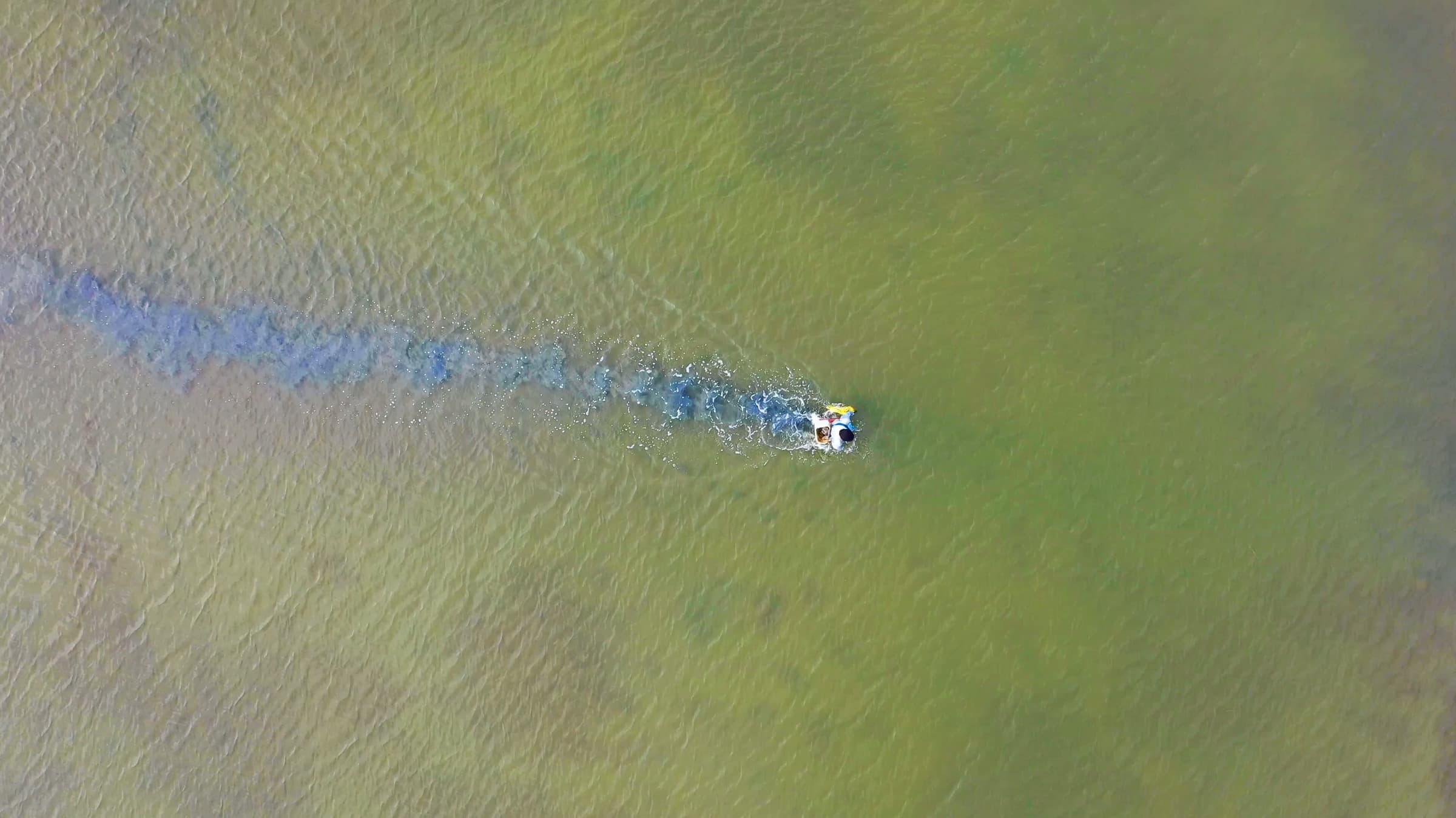 Aerial view of a small boat crossing green-tinted water